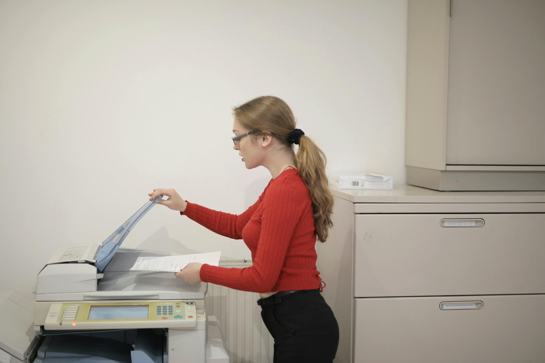 An office employee using a photocopier to copy documents indoors.